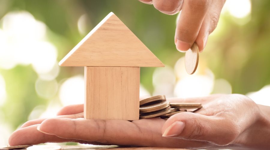 Hand holding miniature house and coins